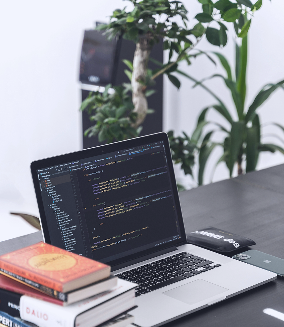 Ordinateur portable affichant du code sur un bureau avec des livres et une plante, illustrant la page contact mobile en cybersécurité